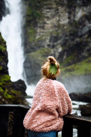 Beautiful girl with a leaf in her hair enjoys a beautiful landscape. Tourist looking at the waterfall.の写真素材