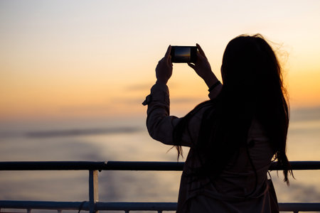 The girl tourist photographs a liner at sunset on the lake in Norway. Tourist takes sunset on the...