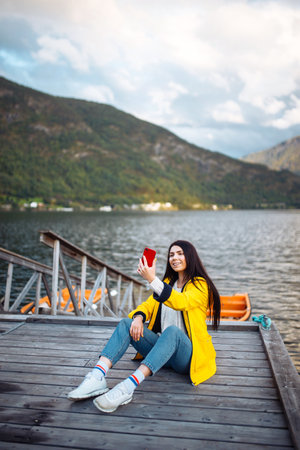 The girl tourist takes a photo on the phone by the lake in Norway. Young woman takes selfie.