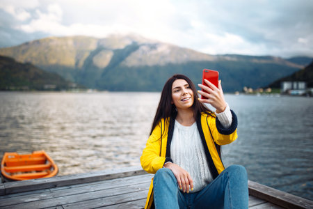 The girl tourist takes a photo on the phone by the lake in Norway. Young woman takes selfie.