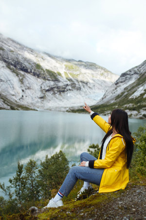 Girl tourist in yellow jacket posing on the lake in Norway. Active woman relaxing in Norway.の写真素材