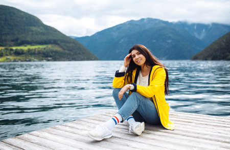 Girl tourist in yellow jacket posing on the lake in Norway. Active woman relaxing in Norway.の写真素材