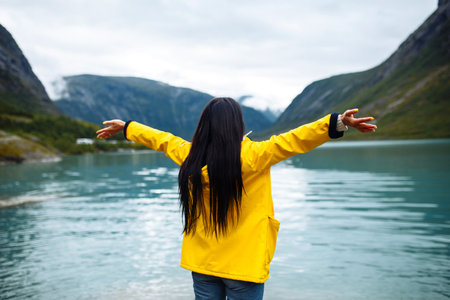 Girl tourist in yellow jacket posing on the lake in Norway. Active woman relaxing in Norway.の写真素材