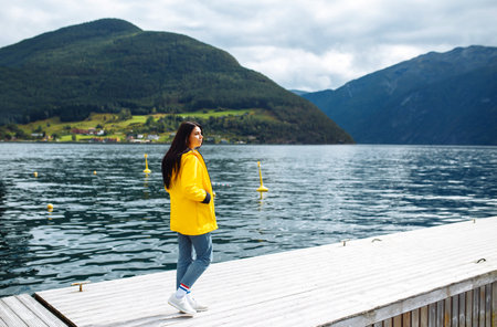 Girl tourist in yellow jacket posing on the lake in Norway. Active woman relaxing in Norway.の写真素材