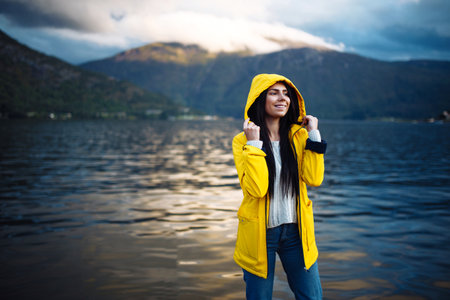 Girl tourist in yellow jacket posing on the lake in Norway. Active woman relaxing in Norway.の写真素材
