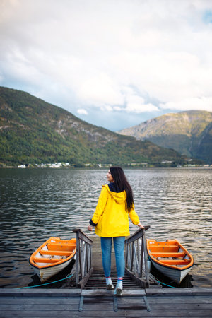 The girl tourist in a yellow jacket posing on the lake in Norway. Traveling, lifestyle, adventure, wild natureの写真素材