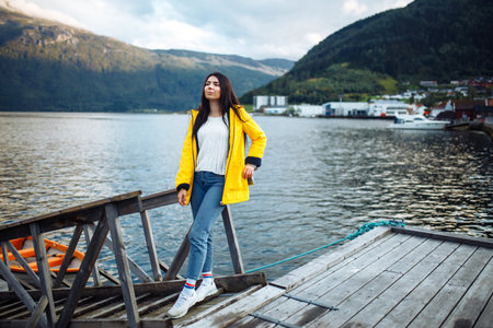 The girl tourist in a yellow jacket posing on the lake in Norway. Traveling, lifestyle, adventure, wild natureの写真素材