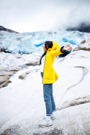 Woman hiking at glacier enjoys freedom. The girl tourist in a yellow jacket near a large glacier, a lot of ice.の写真素材