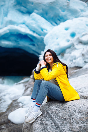 Woman hiking at glacier enjoys freedom. The girl tourist in a yellow jacket near a large glacier, a lot of ice.の写真素材