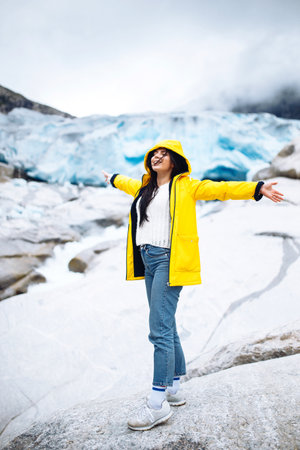 Woman hiking at glacier enjoys freedom. The girl tourist in a yellow jacket near a large glacier, a lot of ice.の写真素材