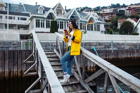 Young woman walking and using a smart phone in the street in a sunny summer day on the street of Norway.の写真素材