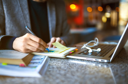 Shot of young male student sitting at table and writing on notebook. Male student studying in cafe.の写真素材