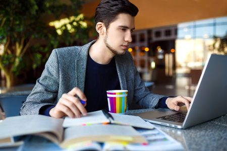 Shot of young male student sitting at table and writing on notebook. Male student studying in cafe.の写真素材
