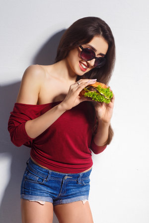 Young beautiful girl with a burger in her hands. studio shot. Model. fast food meal.の写真素材