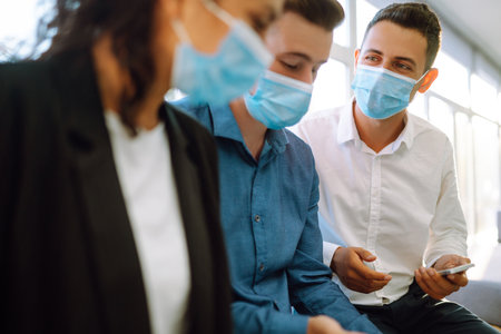 Business colleagues in protective face masks in modern office discussing together work issues.