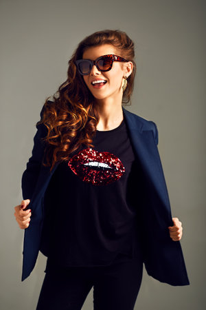 beautiful young girl wearing a jacket, shirt and pants posing on a gray background. studio...