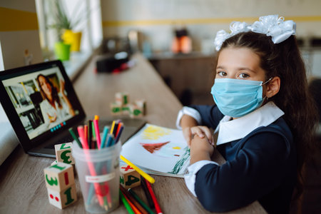 School girl in medical mask using laptop computer studying through online e-learning system.
