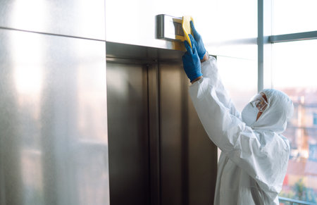 Cleaning and disinfection of the elevator to prevent COVID-19. Worker wearing protective suit sprays.の写真素材