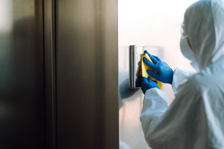 Cleaning and disinfection of the elevator to prevent COVID-19. Worker wearing protective suit...