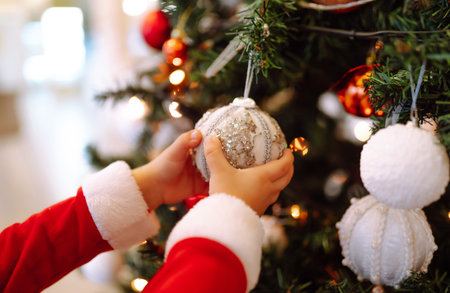 Little child hanging decorative toy ball on Christmas tree branch. Cute child in santa costume decorating.の写真素材