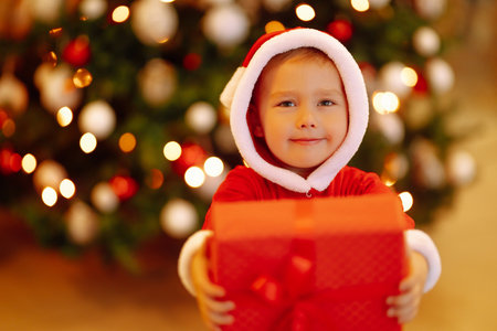 Little boy in santa costume with christmas gift. Happy child holding red present box. new year.の写真素材