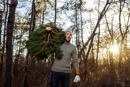 Young man is carrying christmas tree in the wood. men with a beard bears home a Christmas tree.の写真素材