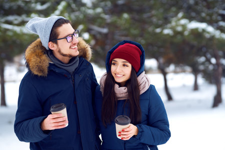winter holidays, hot drinks and people concept. happy young couple with coffee in winter forest.