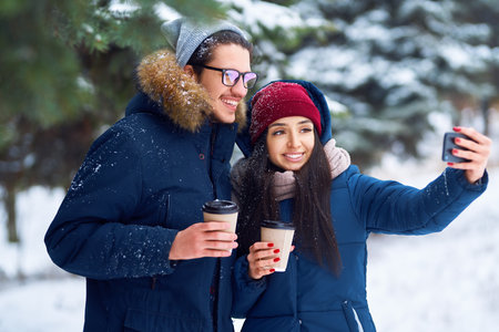 winter holidays, hot drinks and people concept. happy young couple with coffee in winter forest.