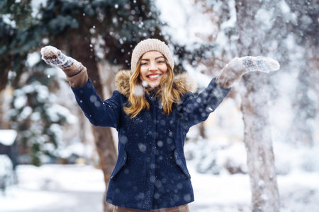 Beautiful girl playing with snow in winter forest. Smiling girl in a blue jacket and knitted hat.の写真素材