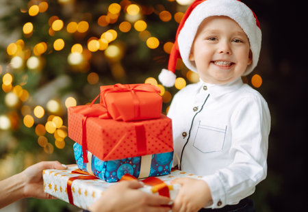 Happy child in Santa red hat receives Christmas gifts.Boy posing with present in Christmas interiorの写真素材