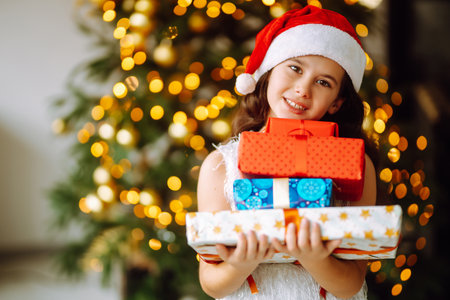 Happy female child in Santa red hat holding Christmas gifts.Smiling little girl posing with presentsの写真素材