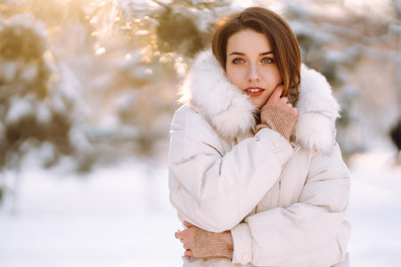 Beautiful woman in winter clothes posing in a snowy park. Young lady walking in a sunny winter day.の写真素材