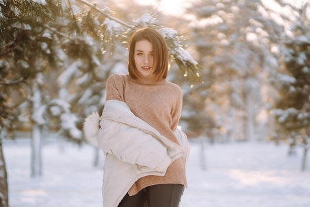 Beautiful woman in winter clothes posing in a snowy park. Young lady walking in a sunny winter day.の写真素材