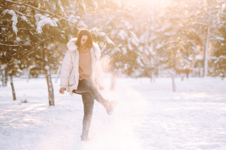 Beautiful woman in winter clothes posing in a snowy park. Young lady walking in a sunny winter day.の写真素材