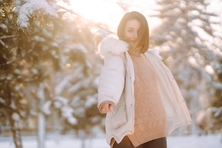 Beautiful woman in winter clothes posing in a snowy park. Young lady walking in a sunny winter day.の写真素材