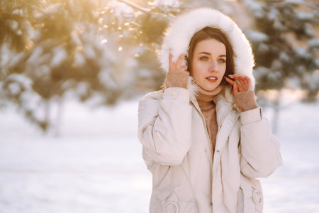 Beautiful woman in winter clothes posing in a snowy park. Young lady walking in a sunny winter day.の写真素材