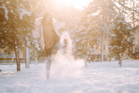Beautiful woman in winter clothes posing in a snowy park. Young lady walking in a sunny winter day.の写真素材