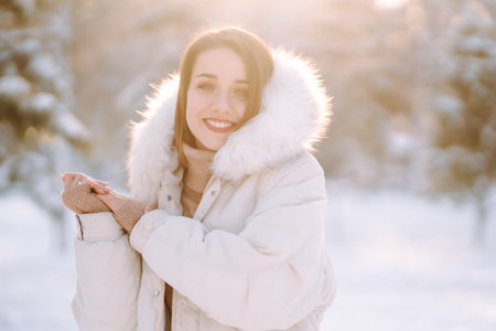 Beautiful woman in winter clothes posing in a snowy park. Young lady walking in a sunny winter day.の写真素材