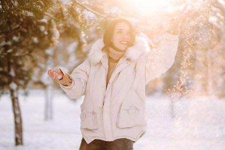 Beautiful woman in winter clothes posing in a snowy park. Young lady walking in a sunny winter day.の写真素材