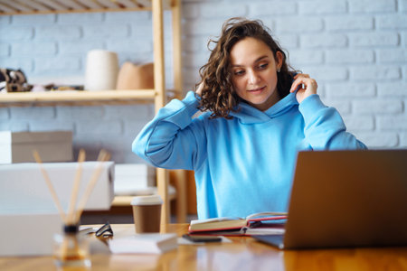Smiling woman takes notes of orders from laptop. Dropshipping owner works.の写真素材