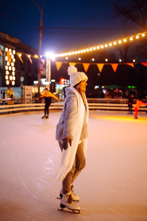 Young woman ice skating on the ice arena in the city square in winter on Christmas Eve. winter holiday.の写真素材