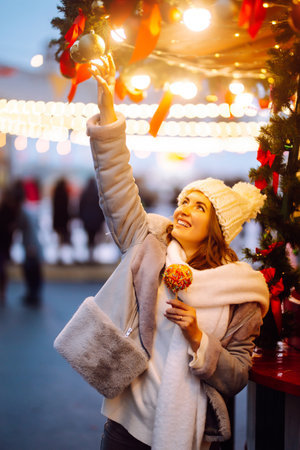 Smiling woman in winter style clothes posing at festive street market. Young woman enjoying winter moments.の写真素材