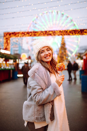 Smiling woman in winter style clothes posing at festive street market. Young woman enjoying winter moments.の写真素材