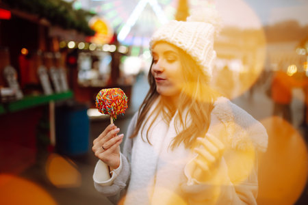 Young woman with caramel apple on Christmas market. Smiling woman in winter style clothes posing.の写真素材