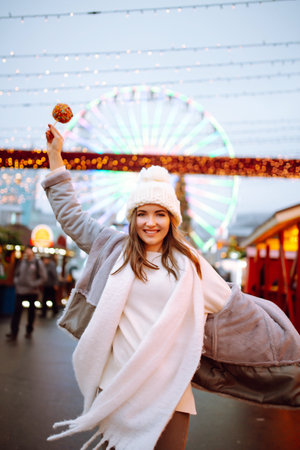Young woman with caramel apple on Christmas market. Smiling woman in winter style clothes posing.の写真素材