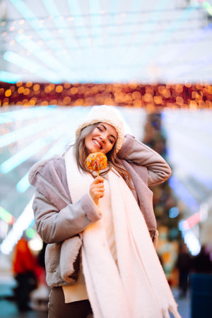 Young woman with caramel apple on Christmas market. Smiling woman in winter style clothes posing.の写真素材