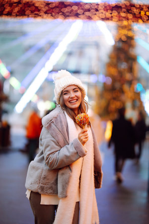 Young woman with caramel apple on Christmas market. Smiling woman in winter style clothes posing.の写真素材