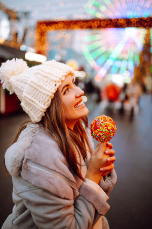 Young woman with caramel apple on Christmas market. Smiling woman in winter style clothes posing.の写真素材