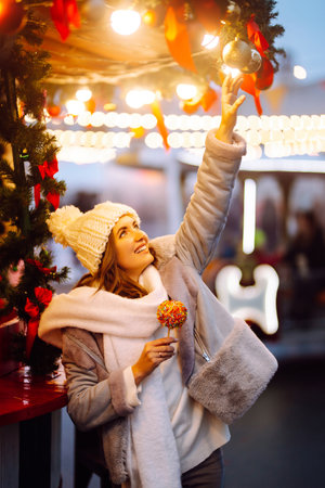 Young woman with caramel apple on Christmas market. Smiling woman in winter style clothes posing.の写真素材