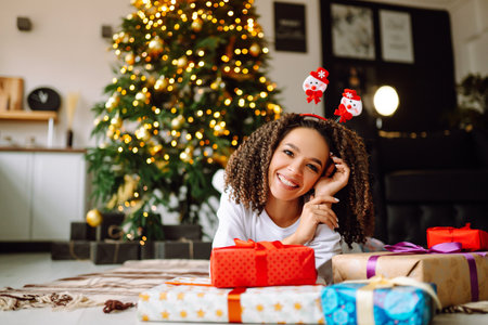 A young woman on the background of a Christmas tree with gifts, with a tablet has a video call or video chat.の写真素材